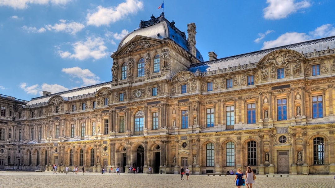 Louvre Museum courtyard with visitors walking on cobblestone.