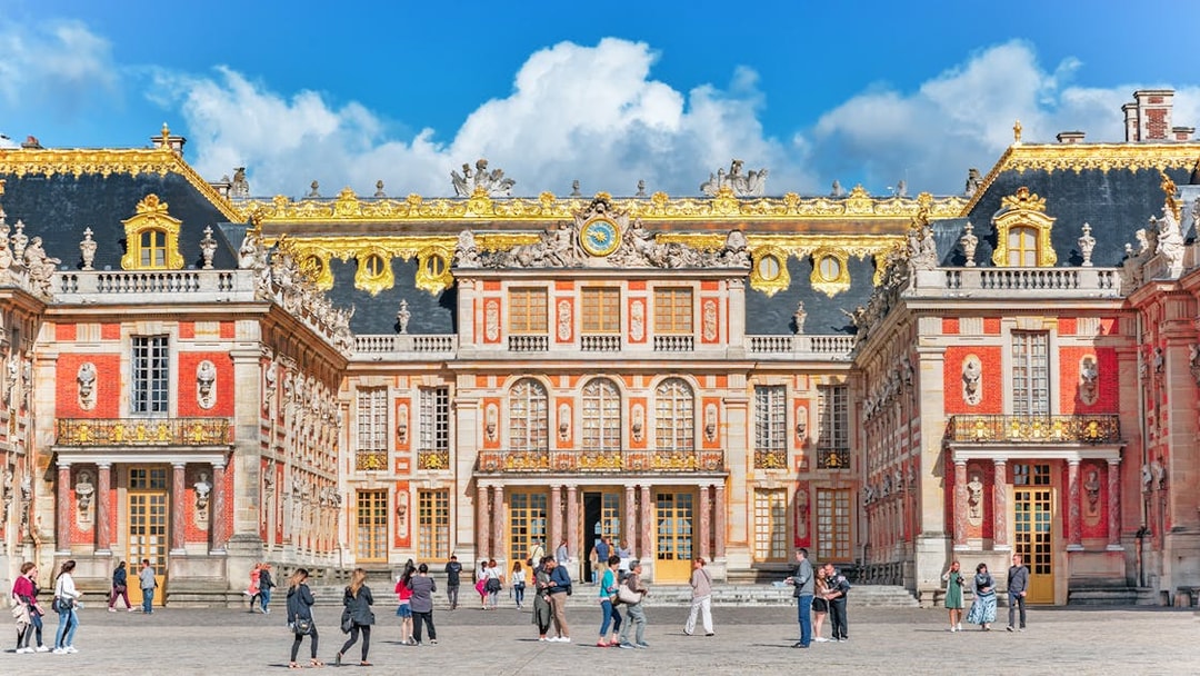 Visitors walking in front of the ornate facade of the Palace of Versailles, France.