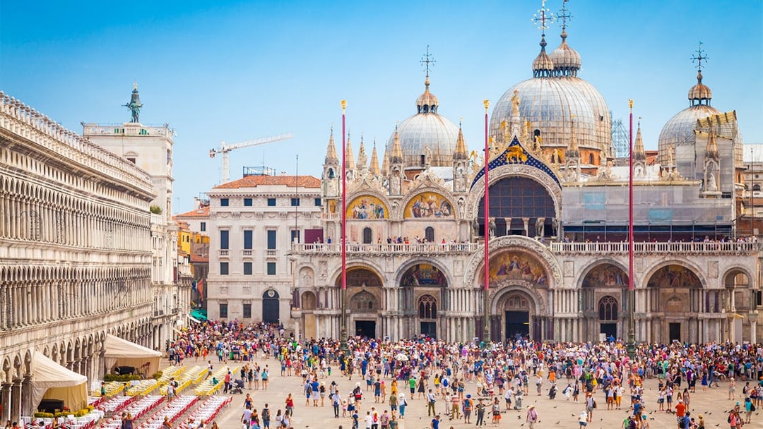 Crowd in front of St. Mark's Basilica, Venice, with ornate domes and arches.