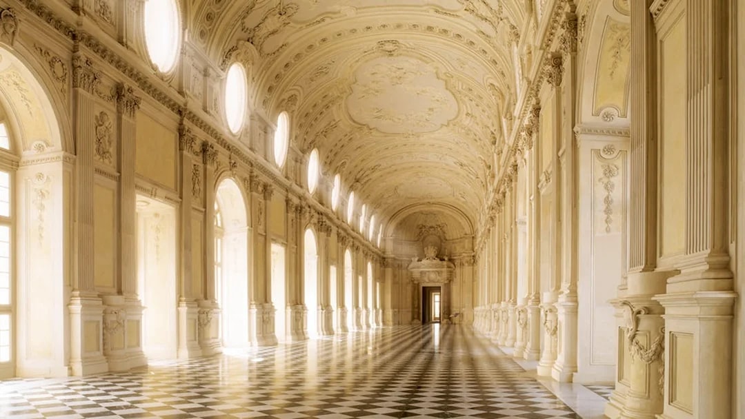 Grand hallway in Turin's Royal Palace with ornate ceiling and checkered floor.