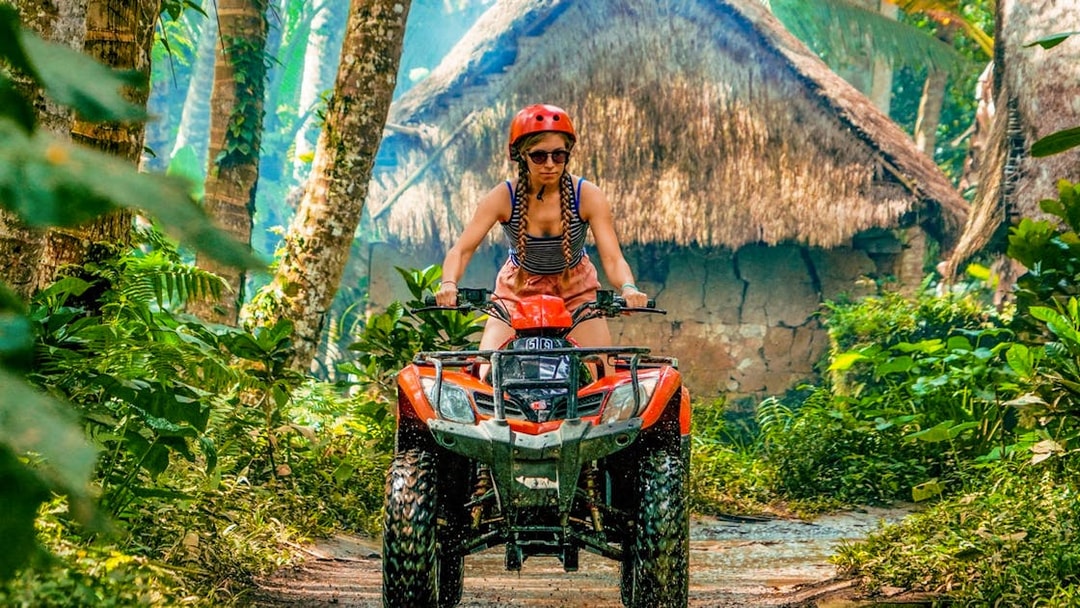 ATV rider navigating jungle path in Ubud with traditional huts in background.