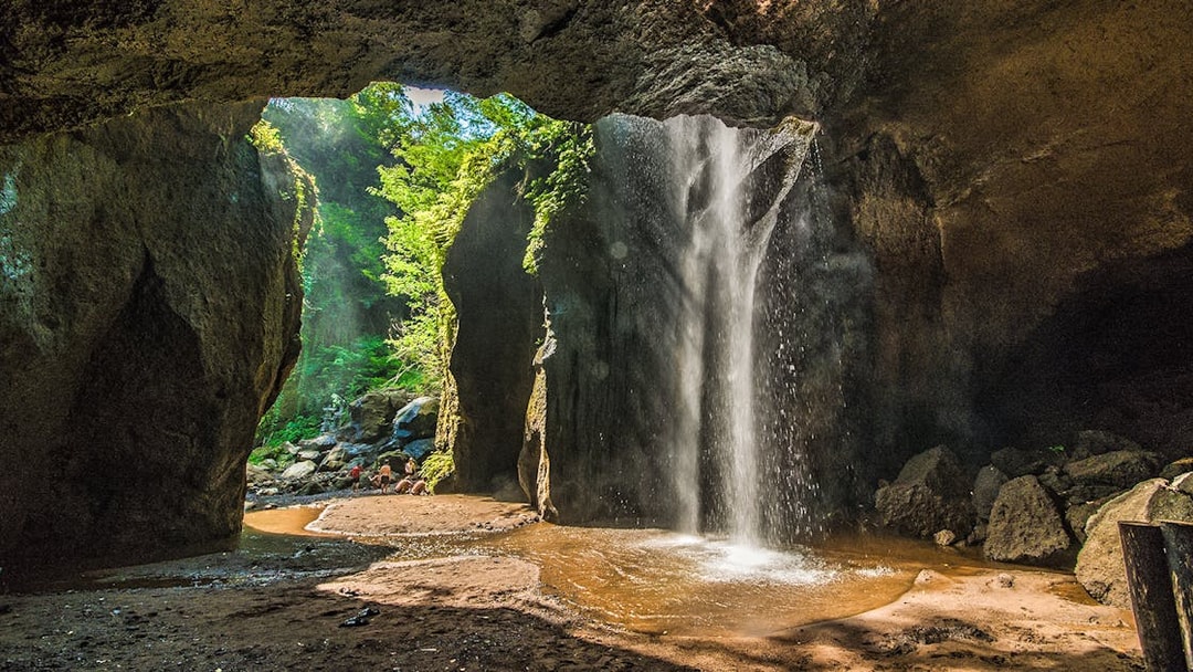 Gushing waterfall inside Goa Raja cave, Ubud, surrounded by lush greenery.