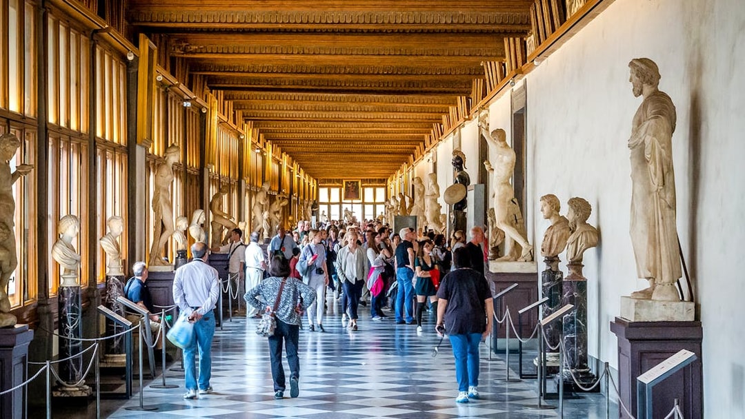 Visitors walking through the statue-lined hallway of the Uffizi Gallery in Florence.