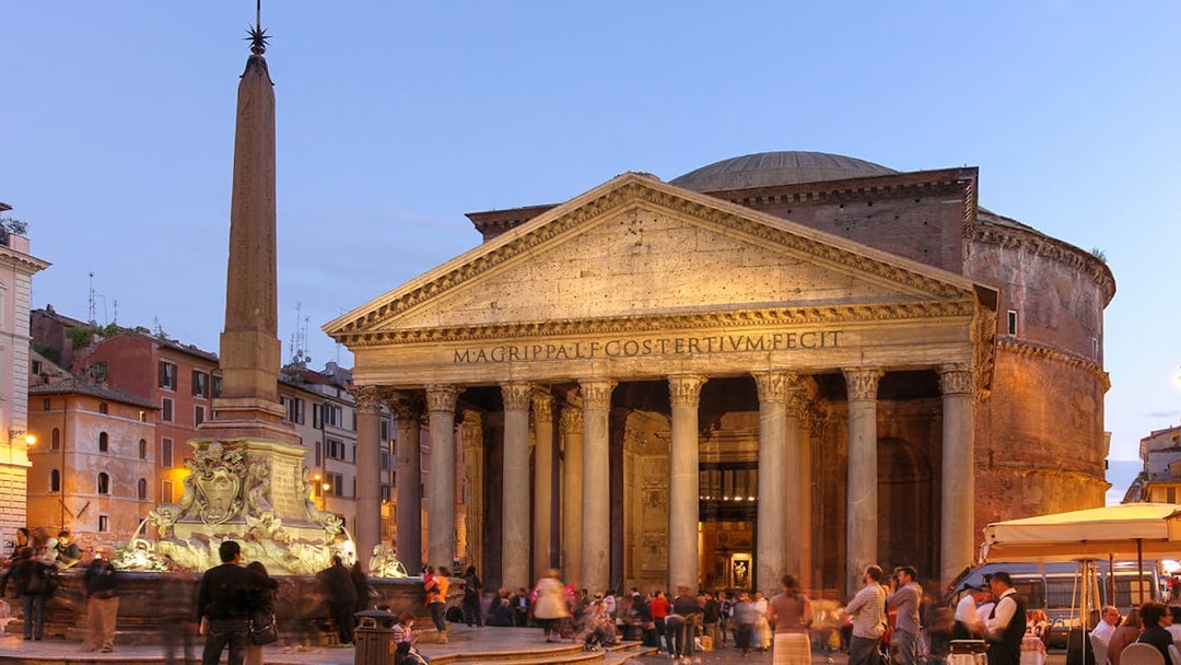 Pantheon in Rome illuminated at dusk with people gathered in the square.