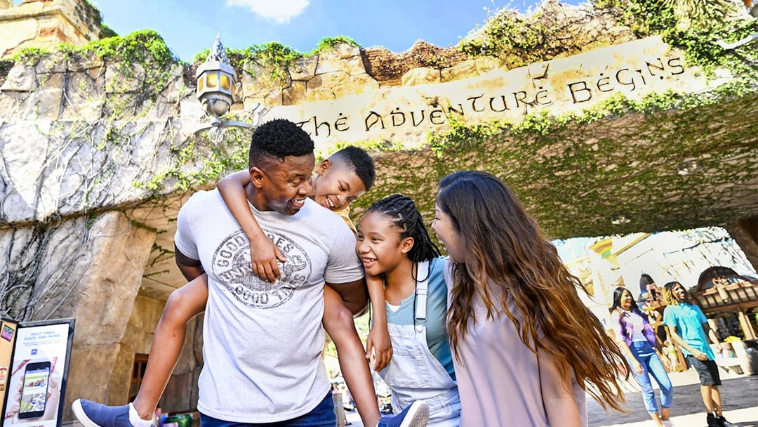 Family smiling under "The Adventure Begins" sign at Universal Studios Resort, Orlando.