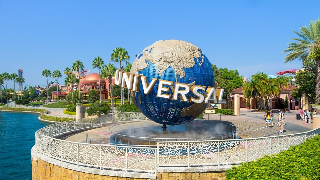 Universal globe at Universal Studios Resort, Orlando, with surrounding palm trees and visitors.