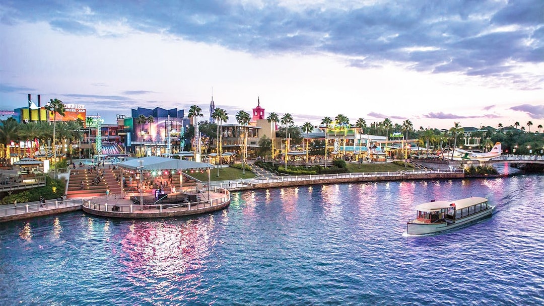 Water taxi on lagoon at Universal Studios Resort, Orlando, Florida, with vibrant cityscape and palm trees.