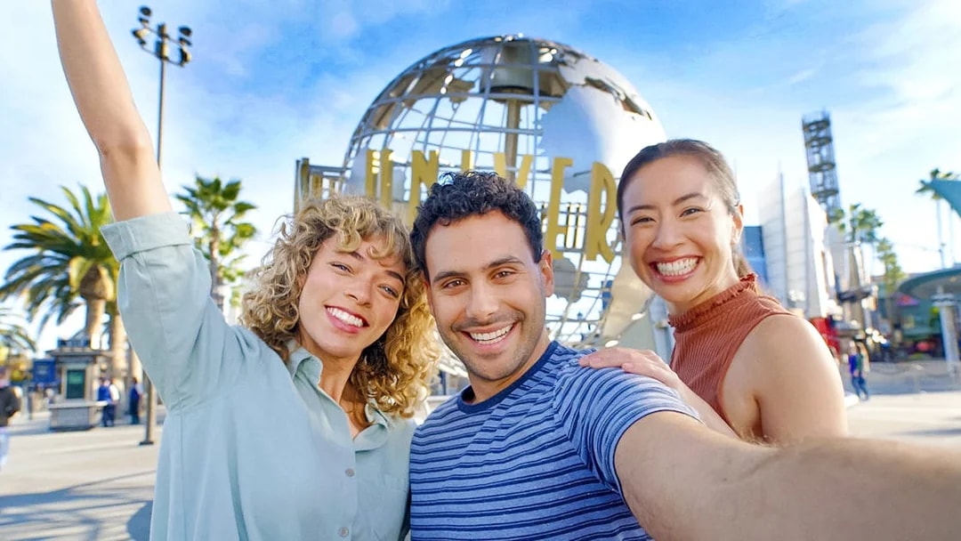 Visitors smiling in front of the Universal Studios Hollywood globe.