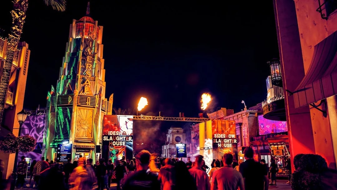 Crowds at Hollywood Horror Nights, Universal Studios Hollywood, with fiery entrance and neon lights.