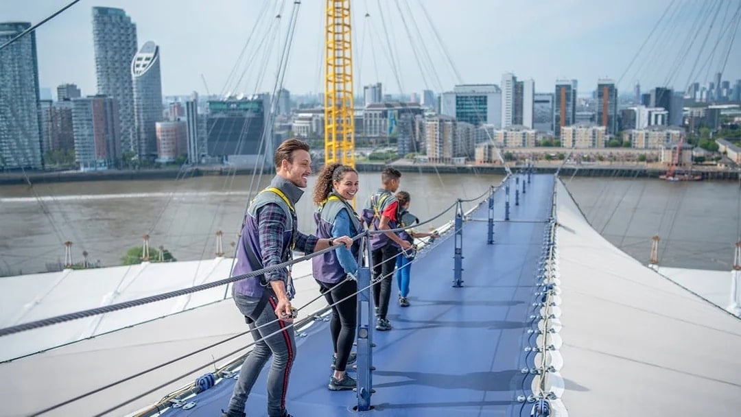 Visitors climbing the O2 roof walkway with London skyline in the background.