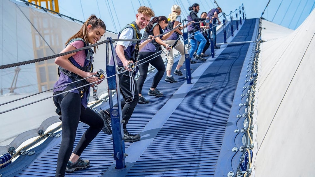 Group climbing the O2 Arena roof in London with safety gear.