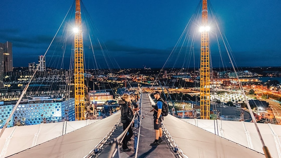 Visitors climbing Up at The O2 during twilight with city lights in the background.