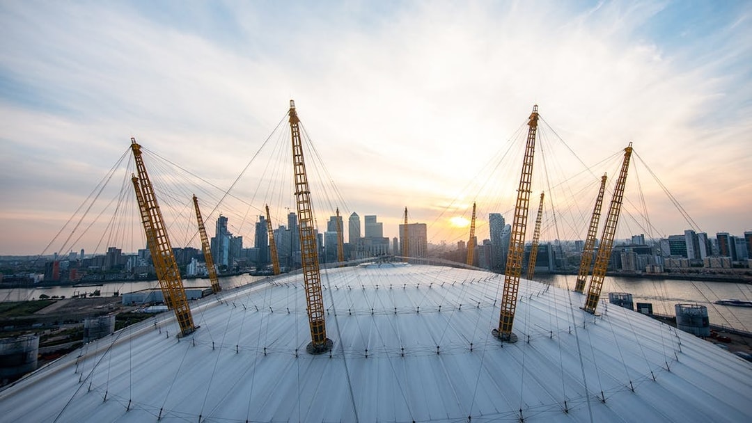 Climbers on the O2 Arena roof in London with city skyline at sunset.