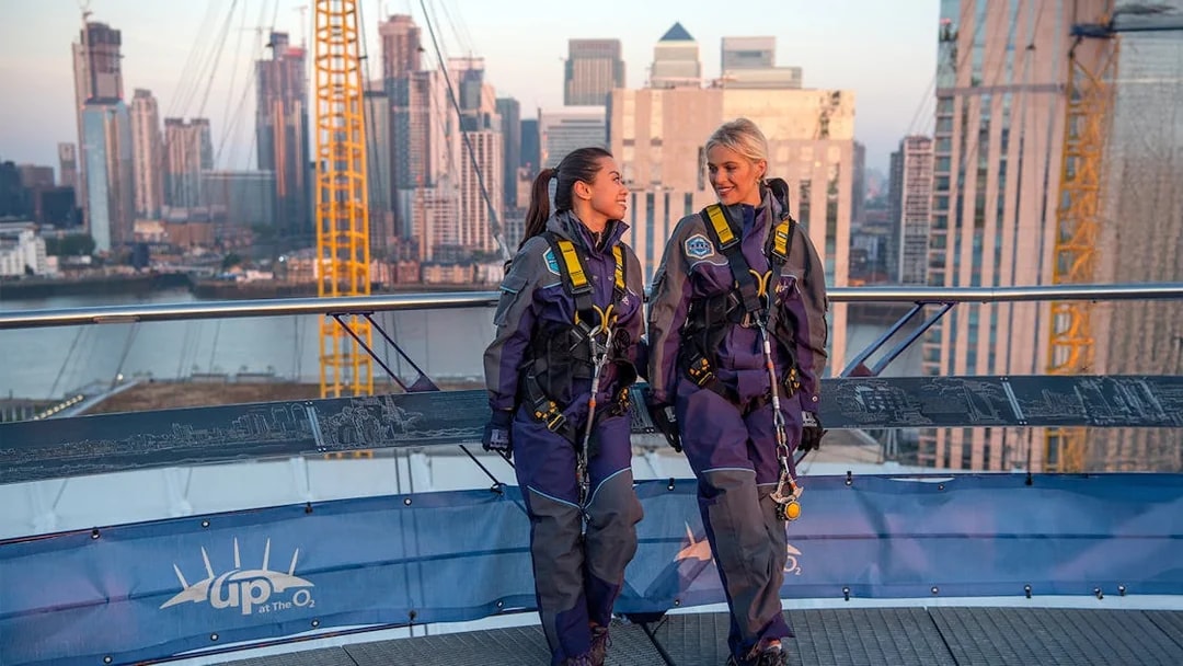 Guests in climbing gear at the O2 Arena rooftop during sunset in London.