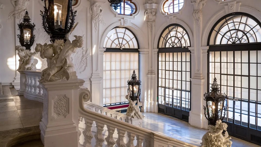 Upper Belvedere Palace interior staircase with ornate sculptures and large windows, Vienna.