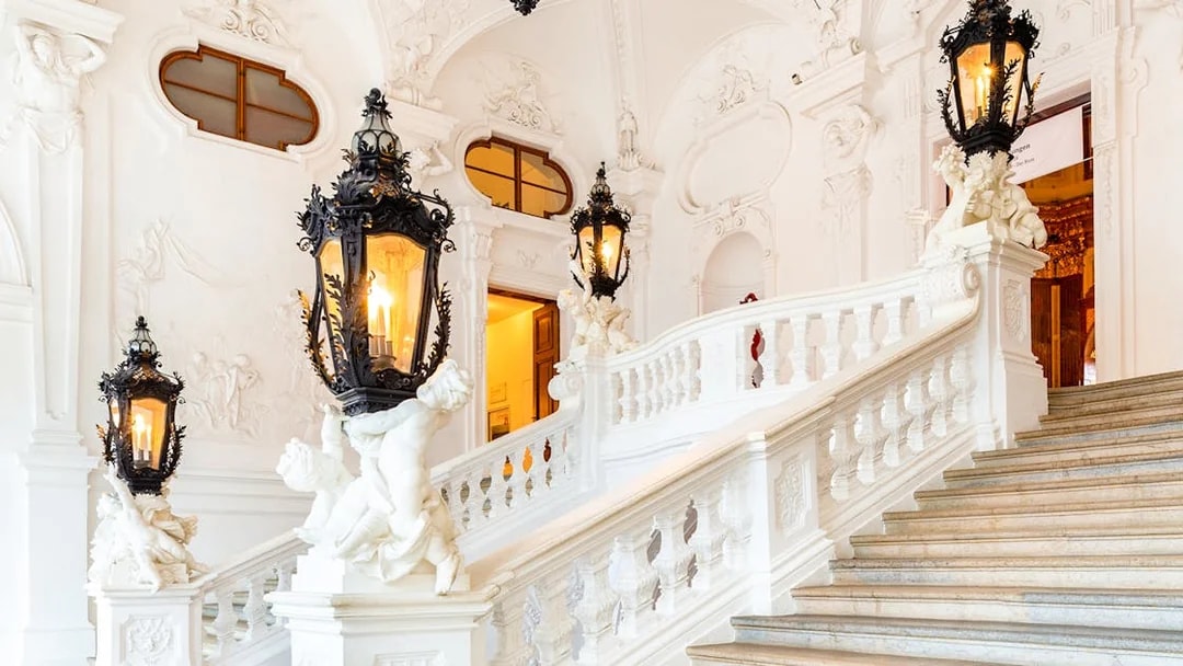 Upper Belvedere Palace interior staircase with ornate lanterns and sculptures.