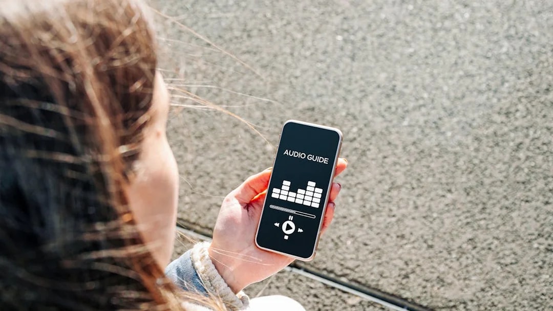 Person holding smartphone displaying audioguide app interface.