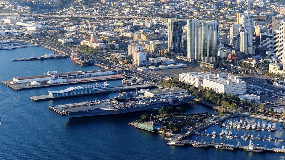 USS Midway Museum aircraft carrier docked in San Diego harbor with city skyline.