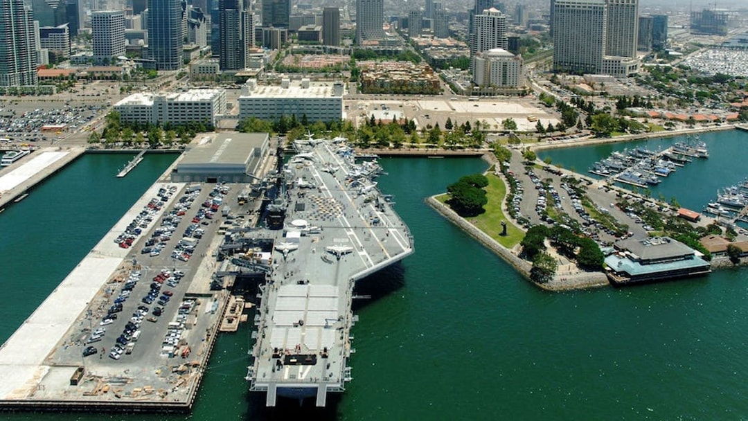 USS Midway Museum aircraft carrier docked in San Diego harbor with city skyline.