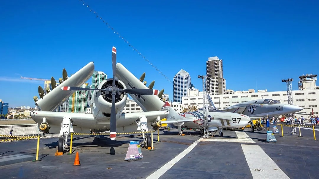 Aircraft display on USS Midway Museum deck, San Diego skyline in background.