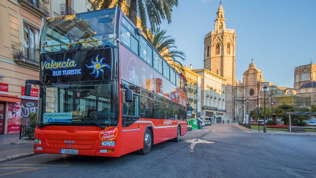 Valencia hop-on hop-off bus near Palma de Mallorca stop with historic buildings in view.