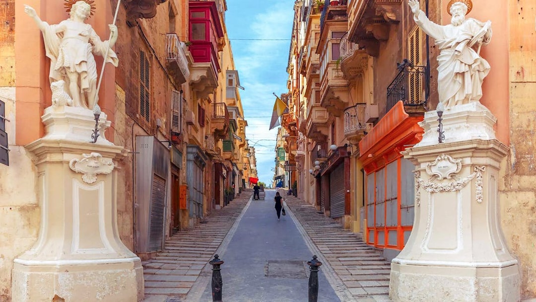 Street view in Valletta with statues and historic buildings.