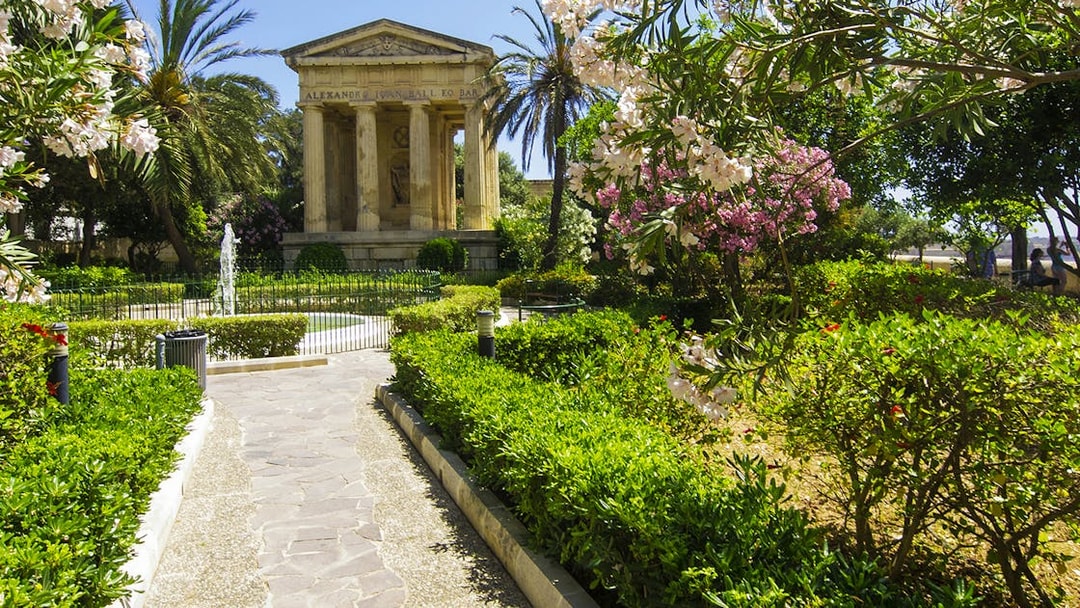 Pathway leading to Lower Barrakka Gardens monument in Valletta, surrounded by lush greenery.