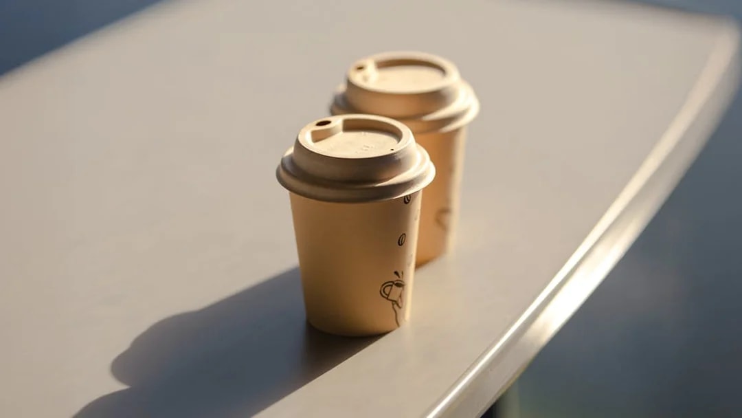 Two paper coffee cups with lids on a table.