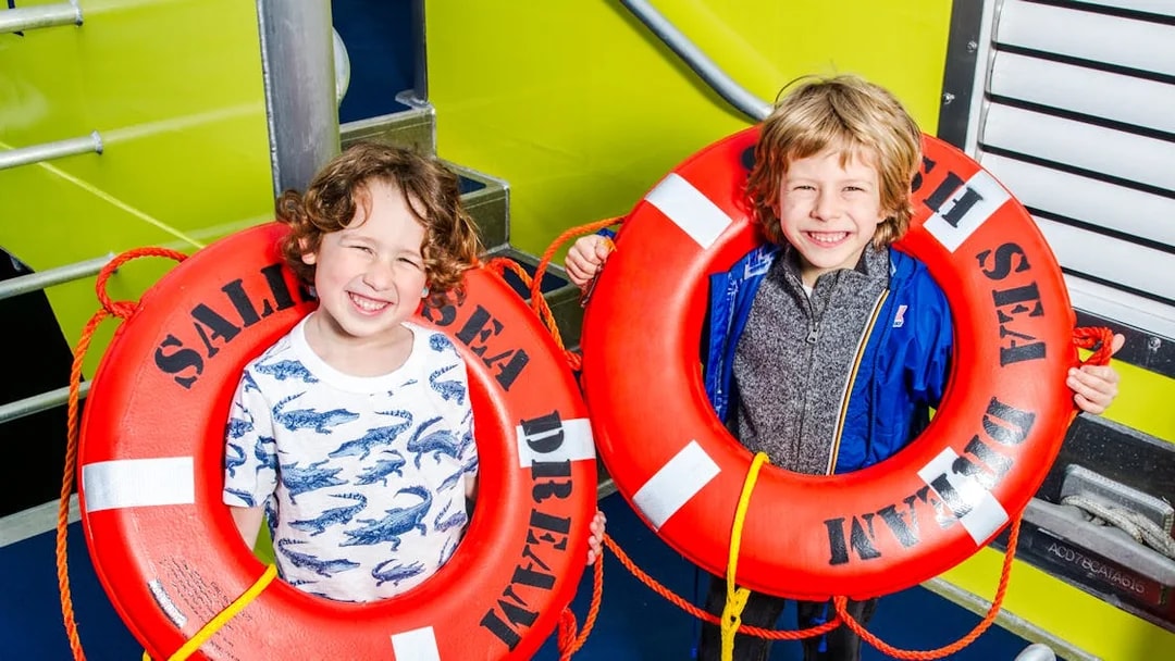 Two children holding red lifebuoys with "Sald Dream Sea" printed on them.