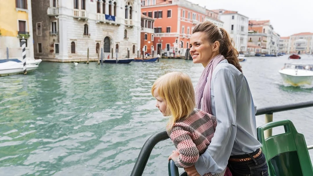 Mother and daughter on Venice water bus with cityscape in background.
