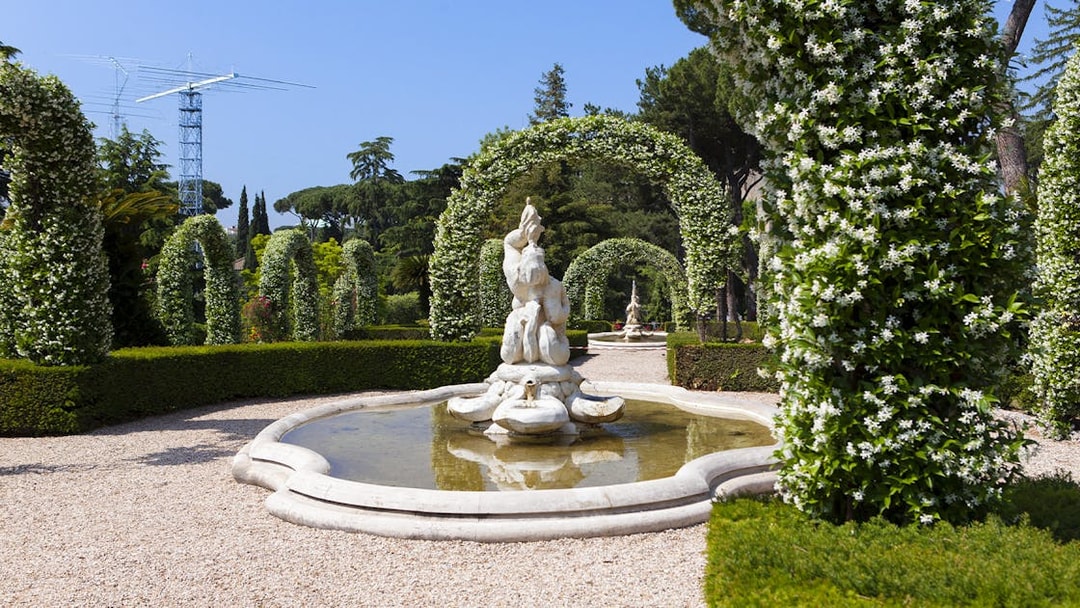 Vatican Gardens fountain surrounded by flowering arches on open bus tour.