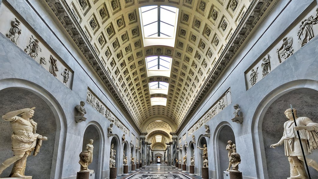 Vatican Museum gallery with classical statues and ornate ceiling.