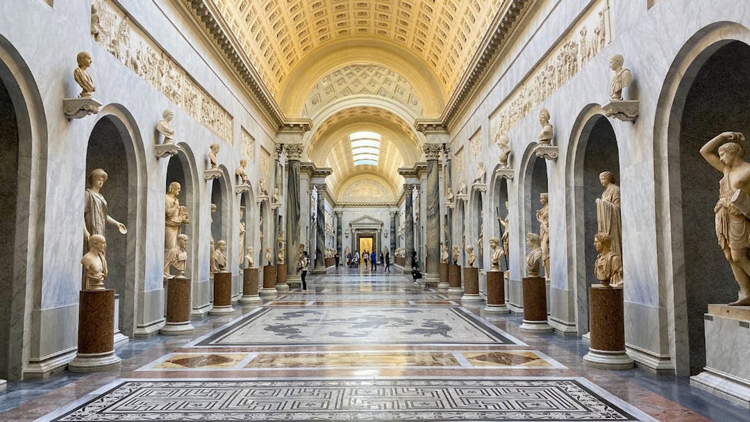 Vatican Museums gallery with classical statues and ornate ceiling.