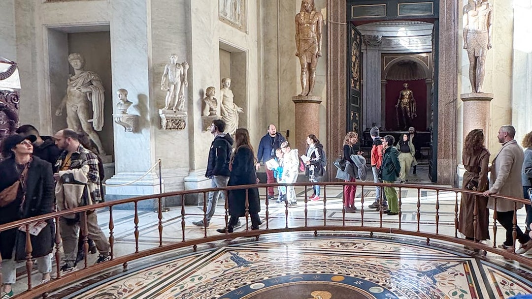 Visitors exploring the Round Hall in the Vatican Museums, Rome, with ancient statues and mosaic floor.