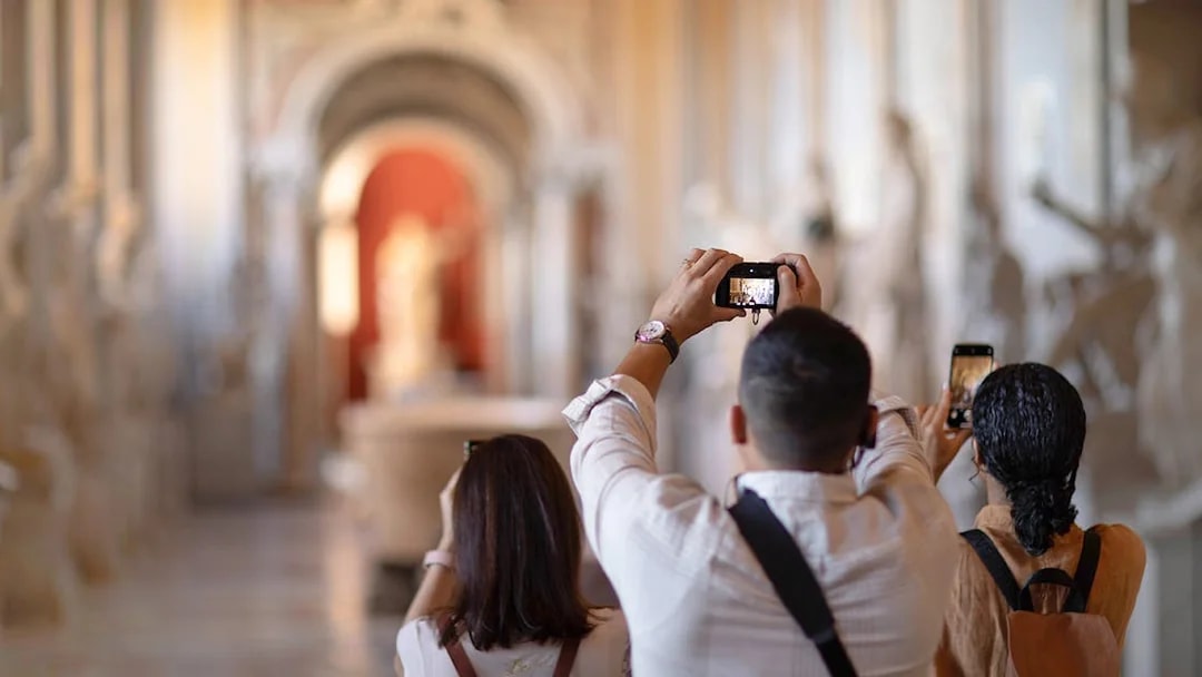 Tourists photographing sculptures in Vatican Museums hallway.