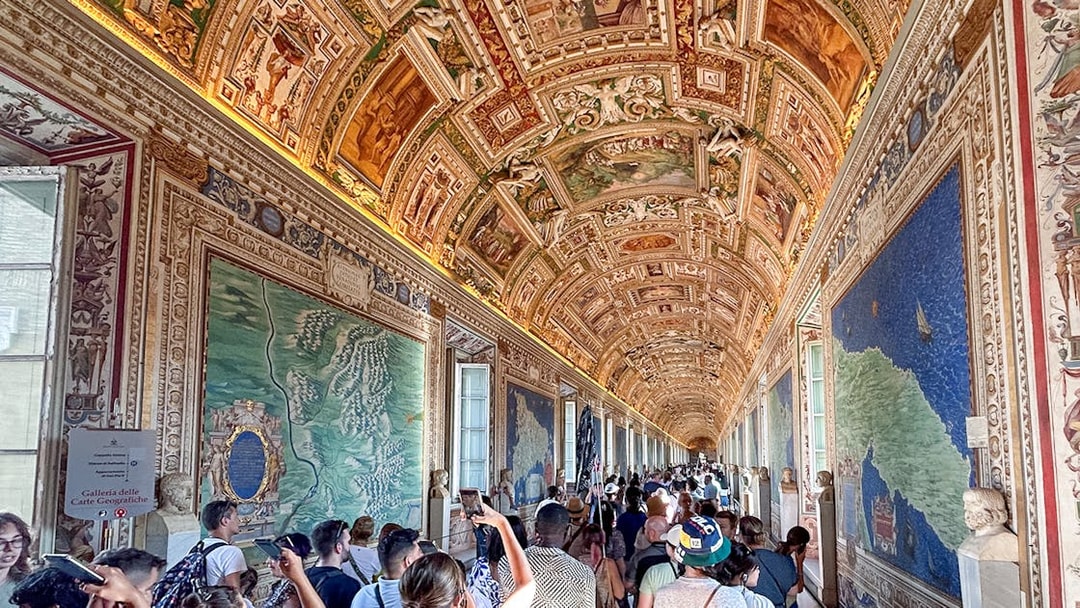 Visitors exploring the Gallery of Maps in the Vatican Museum, admiring detailed frescoes.