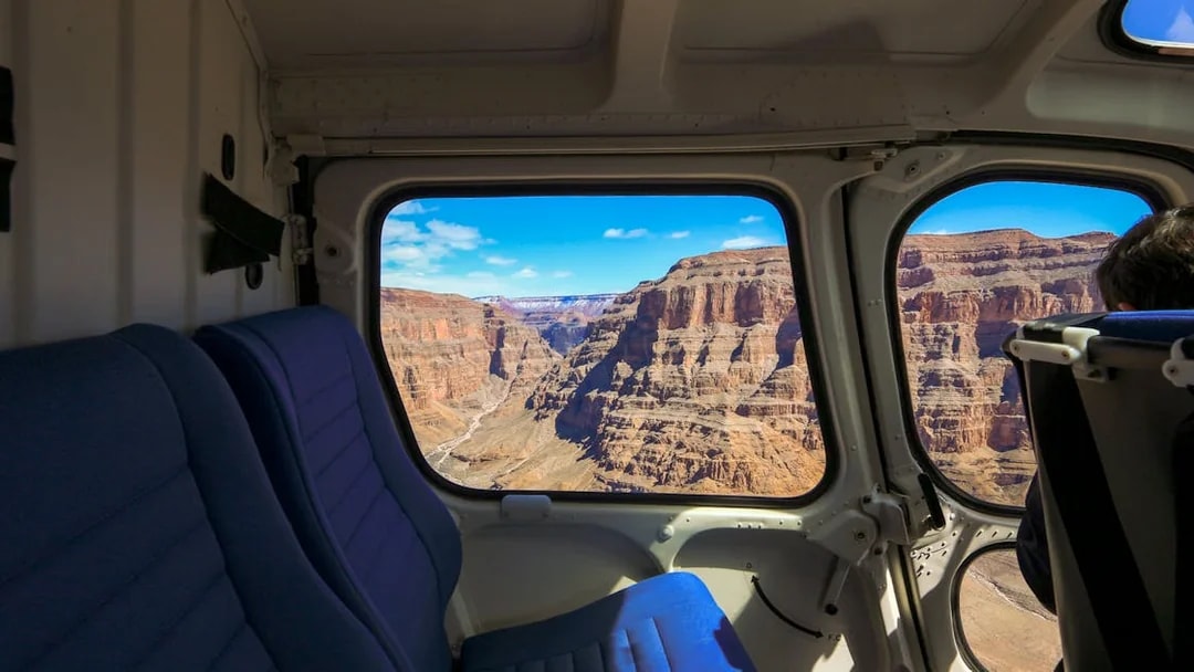 View of the Grand Canyon through a plane window, showcasing rugged cliffs and blue sky.