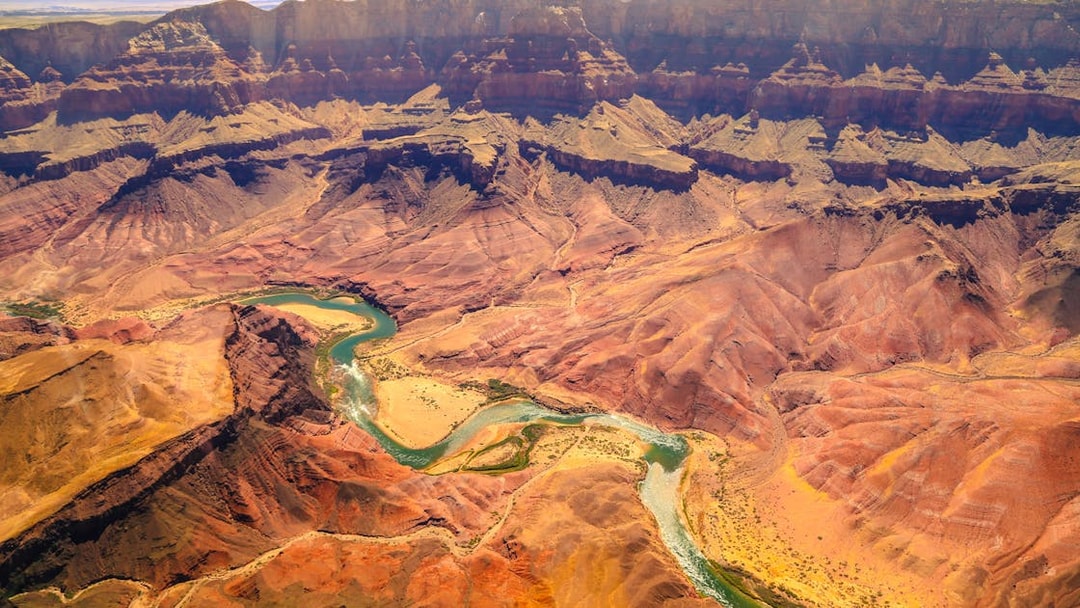 Aerial view of the Grand Canyon with winding Colorado River and layered rock formations.