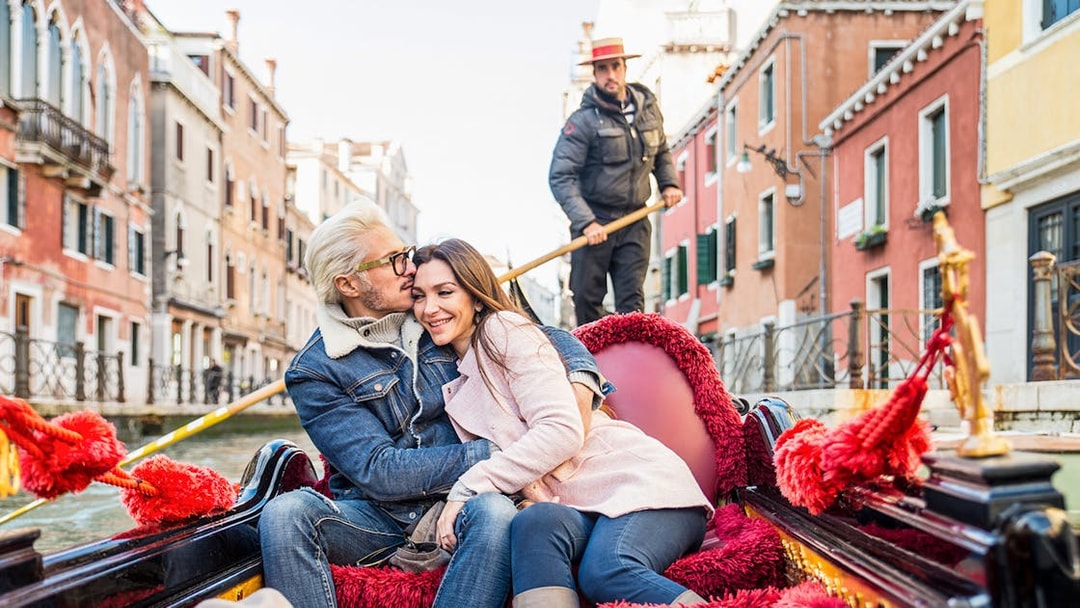 Couple enjoying a gondola ride in Venice canal with gondolier in the background.
