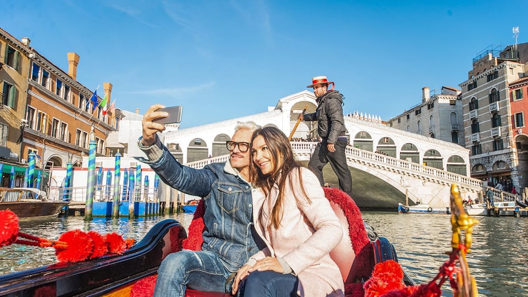 Couple taking selfie on gondola near Rialto Bridge, Venice.