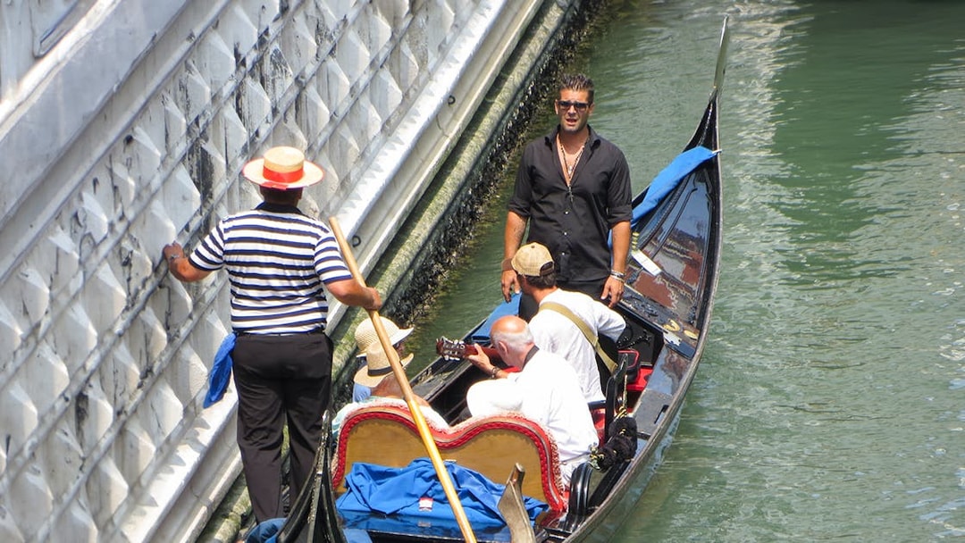 Gondolier steering a gondola with passengers enjoying a serenade in Venice canal.