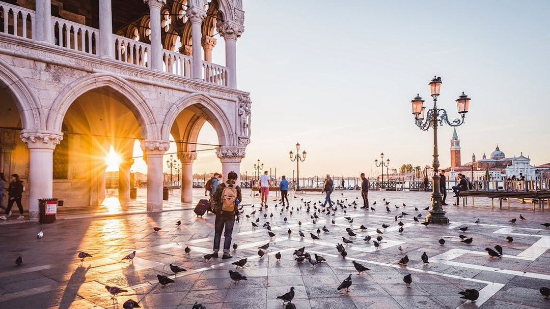 Venice sunrise at St. Mark's Square with people and pigeons, near Doge's Palace.