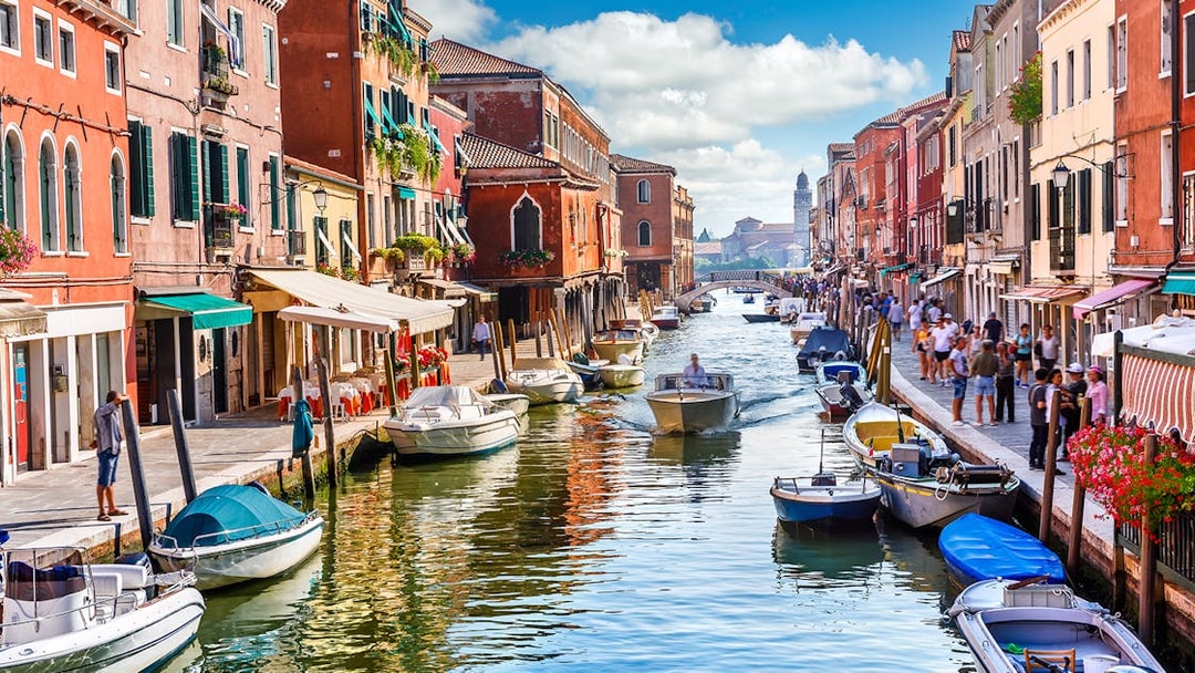 Venice canal with boats and colorful buildings, part of a self-guided audio tour.