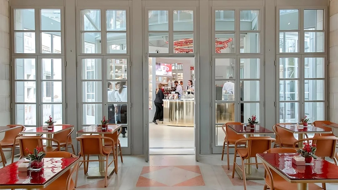 Elegant indoor seating area with red tables and chairs, overlooking a bar in Venice's Royal Garden.