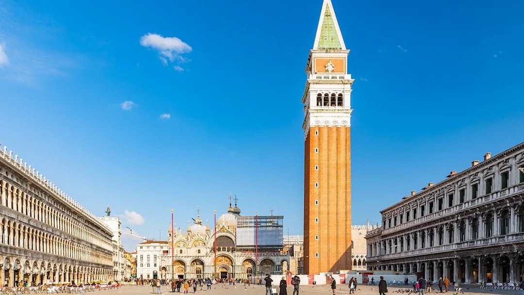 St. Mark's Basilica and Campanile in Venice, Italy, with tourists in the square.