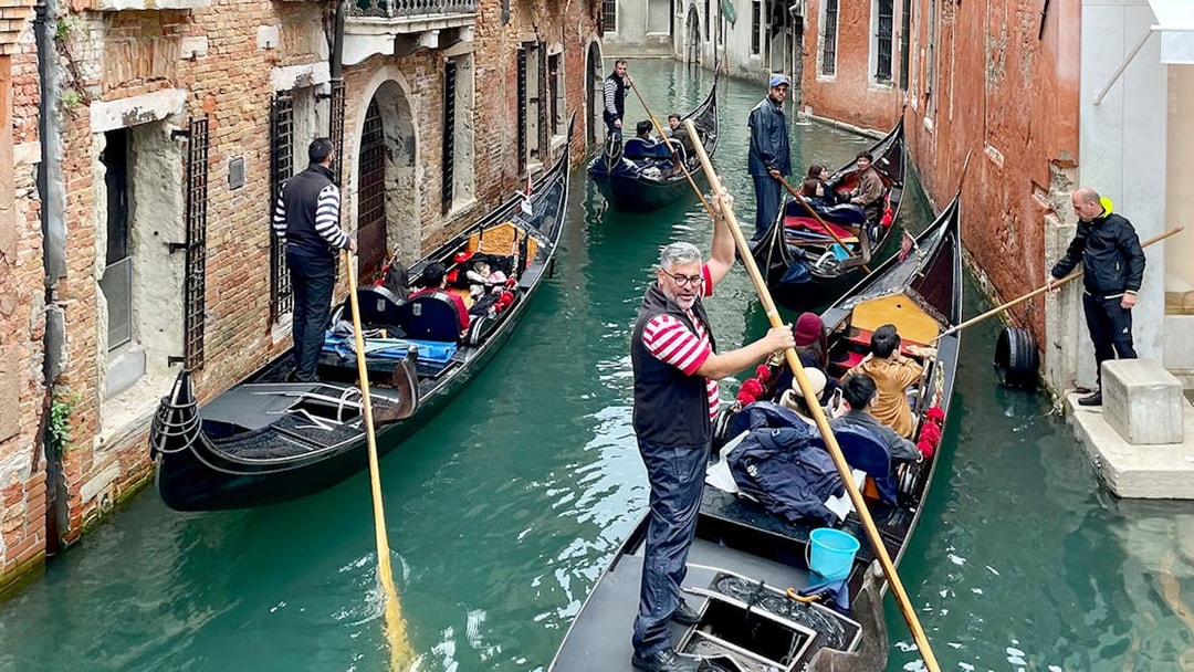 Gondoliers navigating gondolas through a narrow canal in Venice.