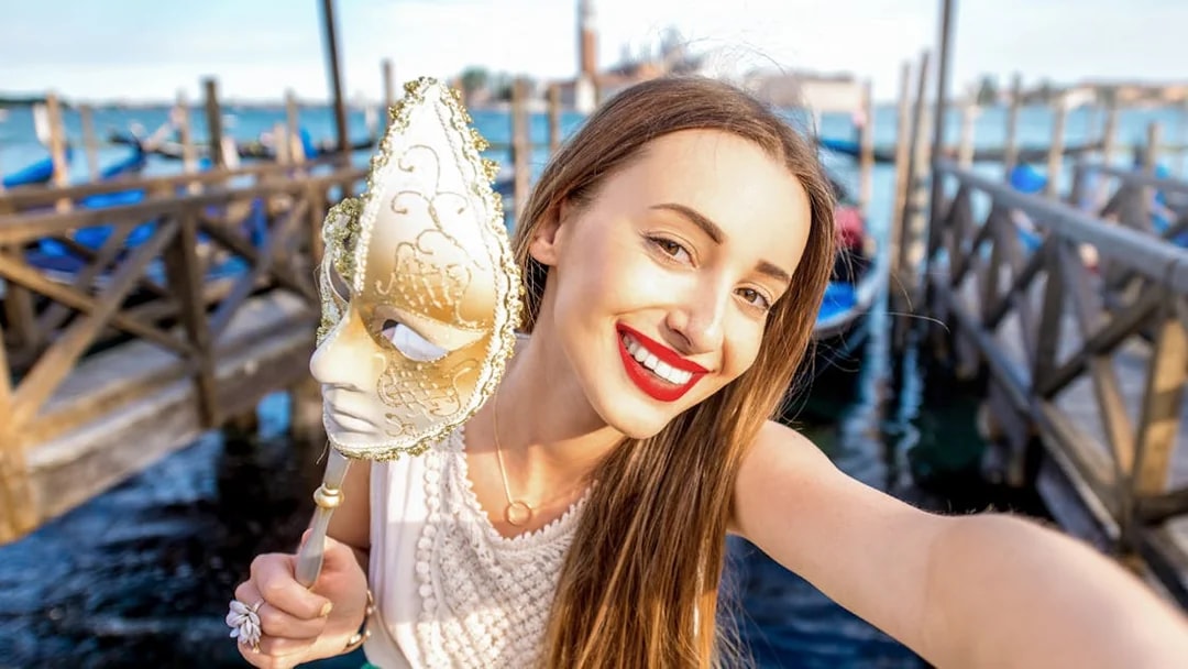Woman holding a Venetian mask near gondolas on a Venice walking tour.
