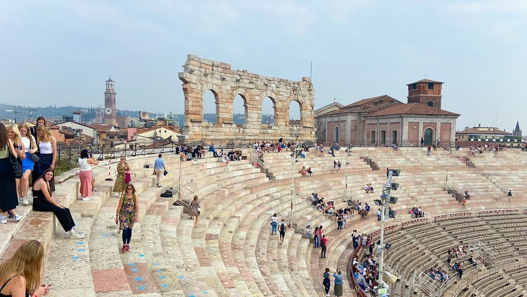 Verona Arena arches with visitors seated on ancient stone steps.