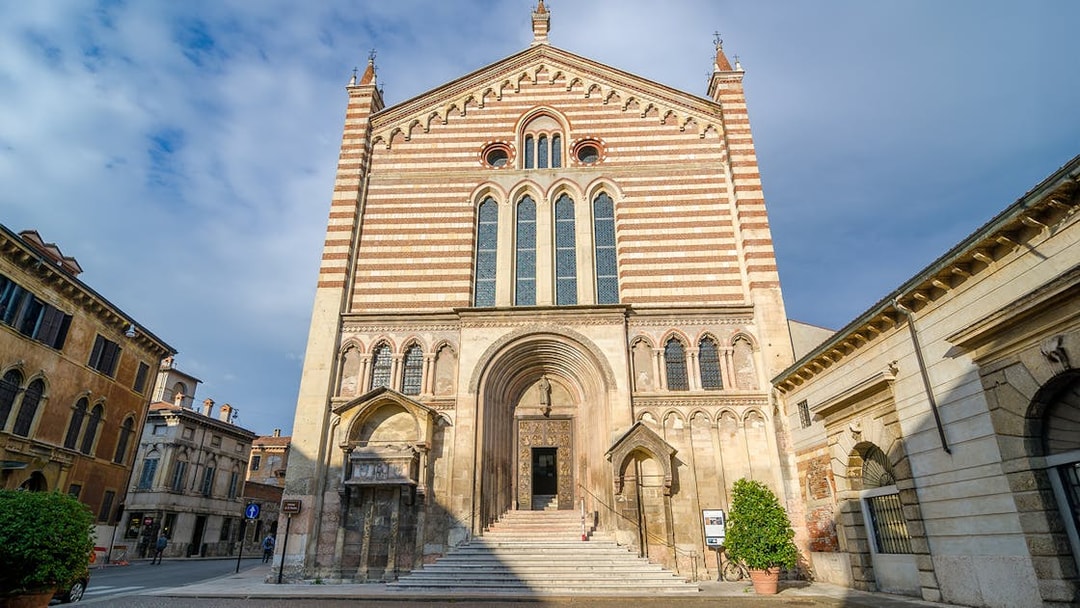 San Fermo Maggiore church facade in Verona, Italy, with striped brickwork and arched entrance.