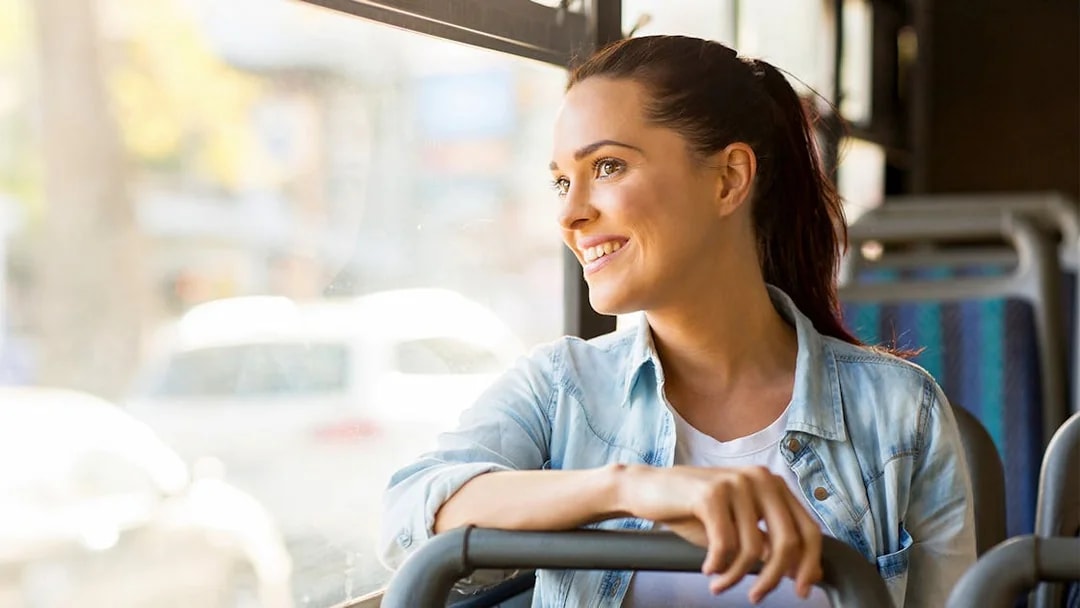 Young woman smiling while riding a bus, looking out the window.